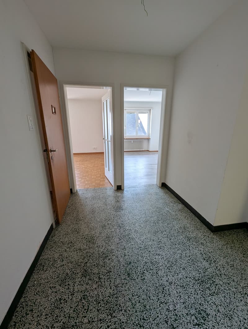 Empty room with white walls, wooden floor, and a window with a radiator