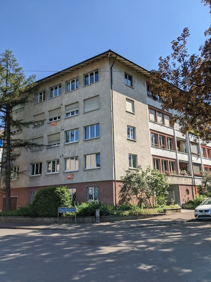 4 story building, multiple windows, red brick base, multiple balconies, trees, plants, car parked