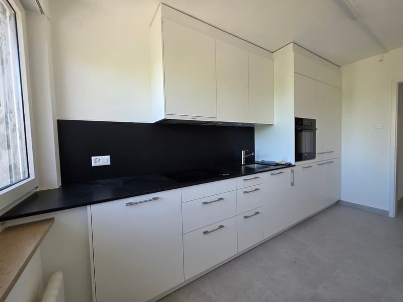 modern kitchen with white cabinets, black countertops, integrated appliances, and a window