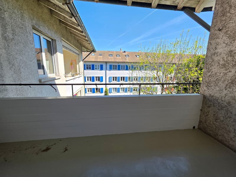 Balcony with railings, concrete floor, view of a building with blue shutters