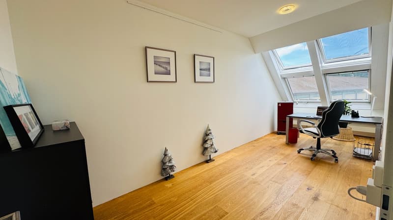 Empty room with wooden floor, ceiling lamps, office chair, desk, window, framed pictures on wall