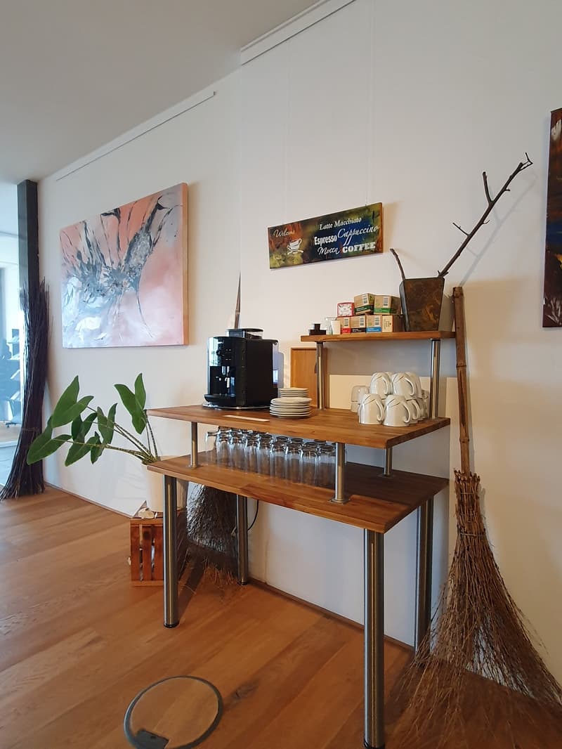 modern styled desk, stack of plates, glasses, cups, broom, coffee machine, potted plant, paintings