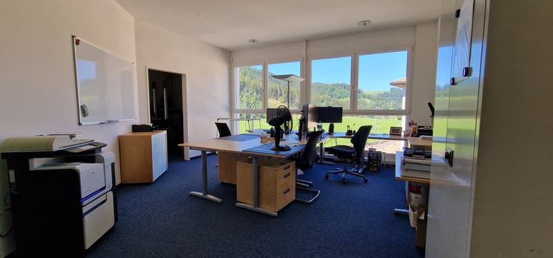 Office room with large windows, desks, computers, printer, filing cabinets, and a whiteboard.