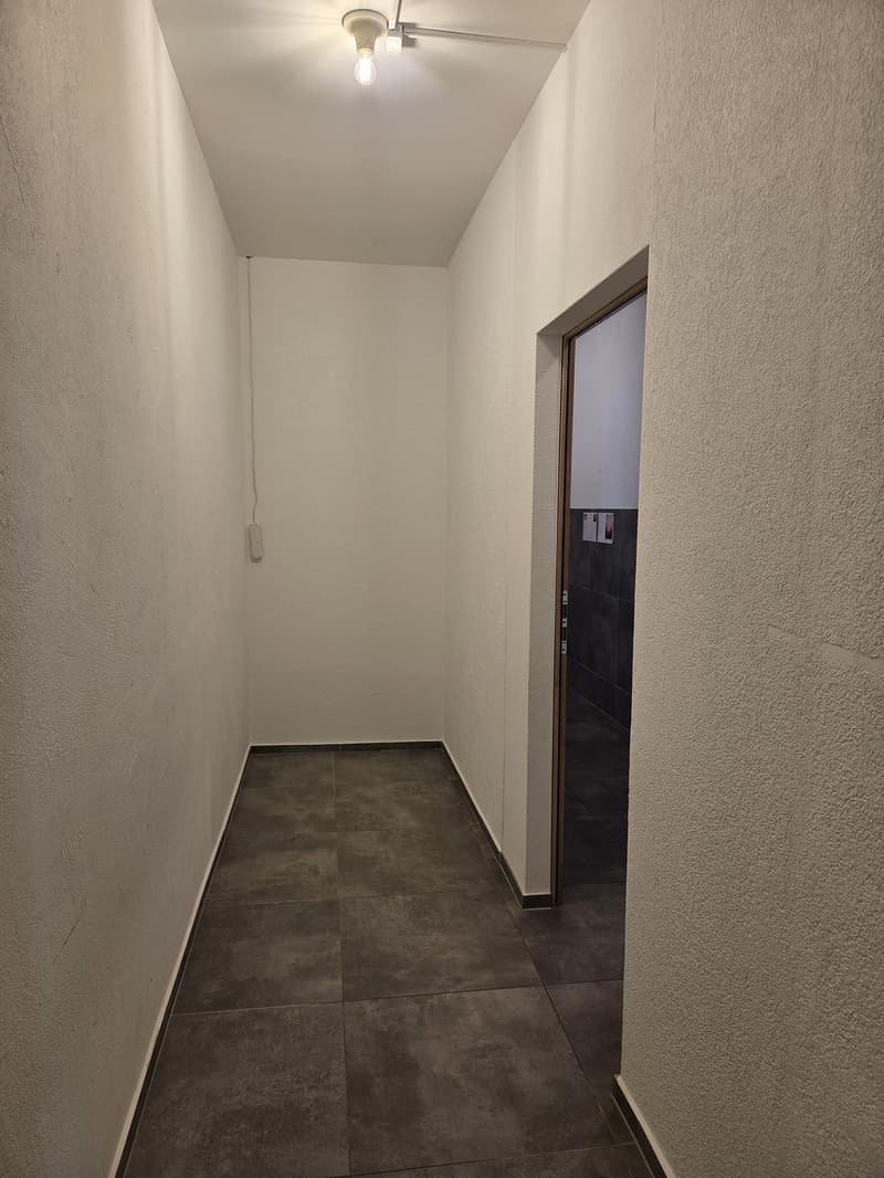 Empty hallway with tiled floor, white walls, and a single light fixture on the ceiling.