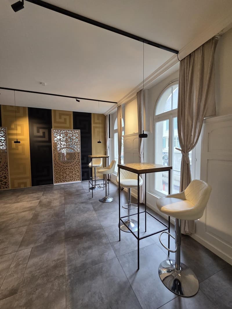modern room with gray tiles, white walls, black and gold wall design, white chairs, wooden tables, large window with curtains
