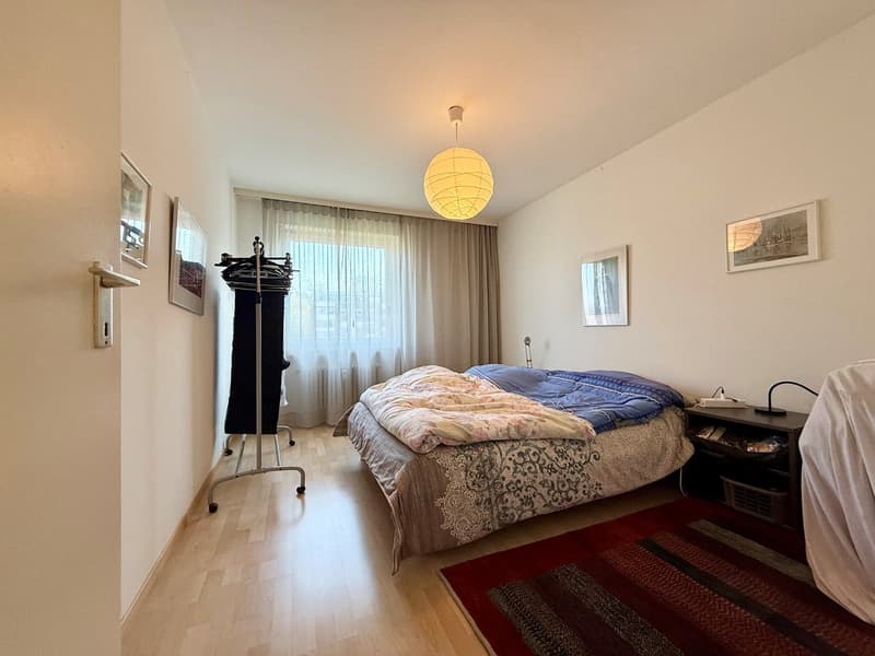 Bedroom with bed, nightstand, rug, lamp, clothes rack, curtains, picture frames, wooden floor