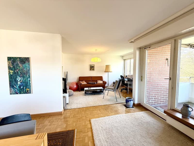 wooden floor, white walls, brown couch, coffee table, lamp, painting, sliding glass doors, balcony