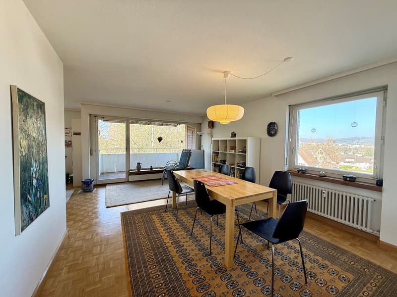 Dining room with wooden table, black chairs, wooden floor, large windows, balcony, radiator, painting, rug