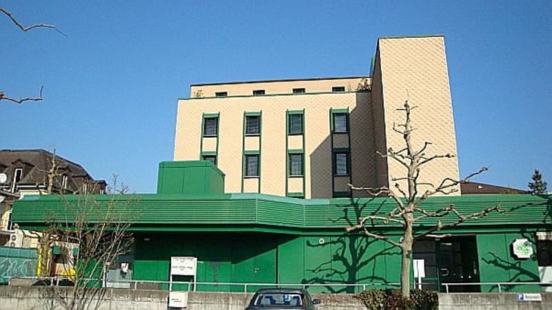 A three-story commercial building, with beige and green exterior, car parked in front