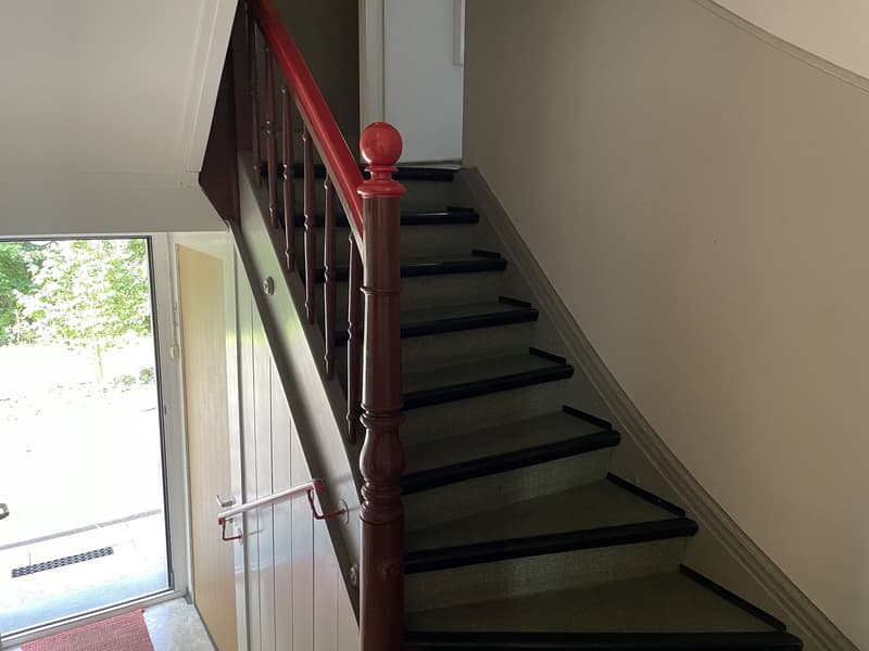 Red handrail, red finial, white wall, black and brown floor, open doorway