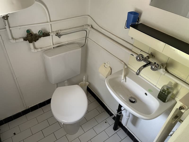 A small bathroom with a white toilet, a sink, and tiled flooring.