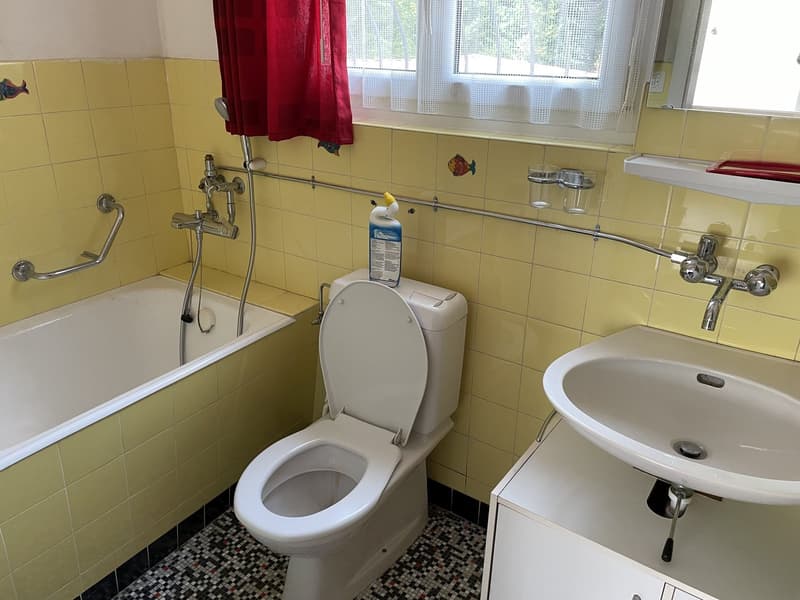Bathtub with handrails, white toilet, white sink, yellow and white tiles