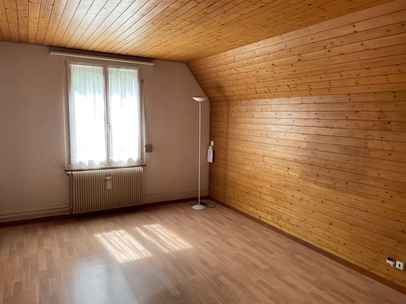 Empty room with wooden walls, floor, and ceiling, a radiator, a window with curtains, and a white floor lamp.