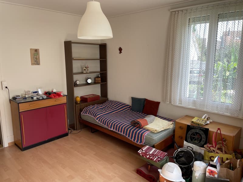 Room has bed, desk, shelf with various items, window with curtains, and a lamp.