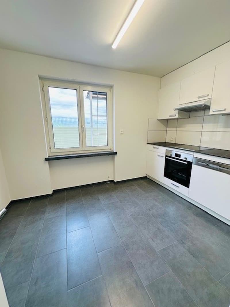 empty kitchen with white cabinets, tiled floor, large window, oven, dishwasher