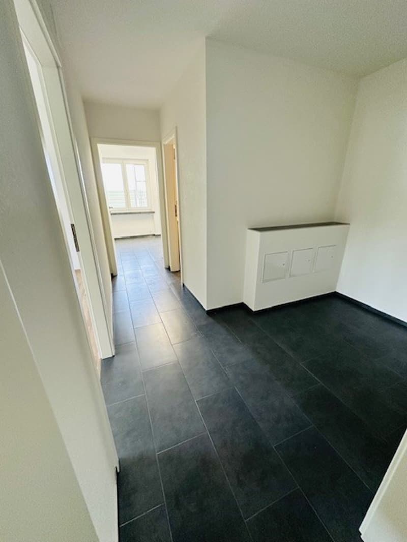 Empty hallway with white walls, black tiles, and a window.