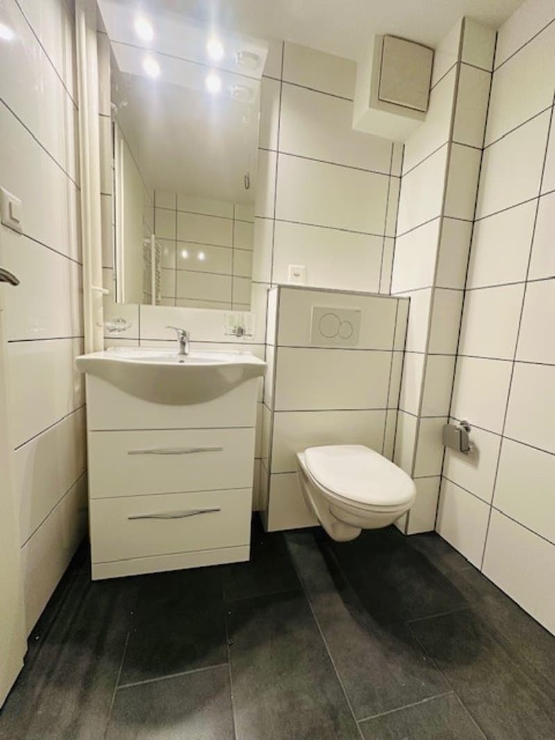 Bathroom with white tiles, white sink, white toilet, mirror, and white cabinet
