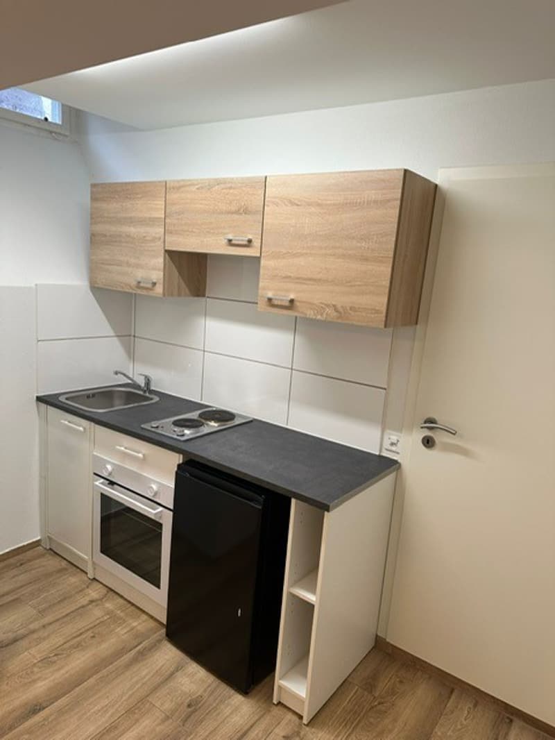 modern kitchen with wooden cabinets, black countertop, stainless steel sink, oven, dishwasher, washing machine, and a window