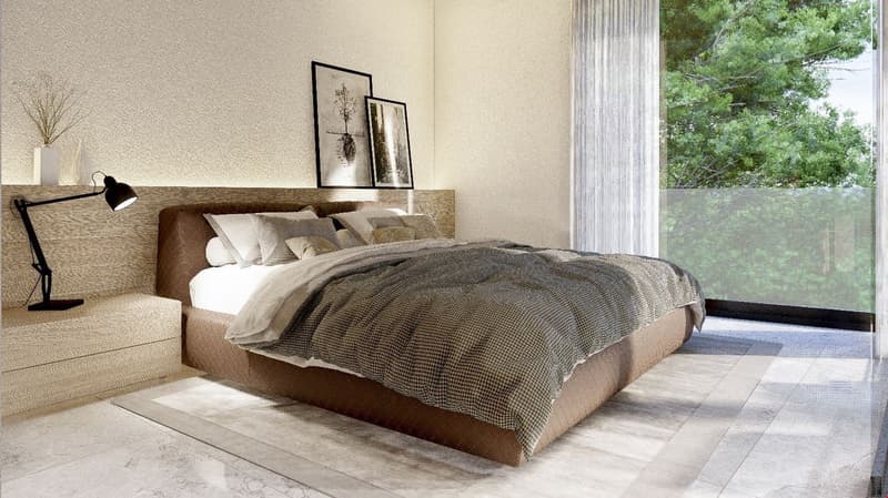 Spacious bedroom with large windows overlooking a wooded area, wooden floor, neutral-colored walls, a wooden bed frame with a plush bedding set, and framed artwork on the wall above the bed. The room also features a reading lamp on a side table.