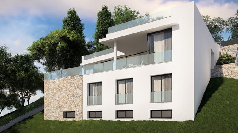 Modern two-story house with white exterior walls, large windows, and a balcony on the upper level. The house is surrounded by trees and has a stone wall on one side.