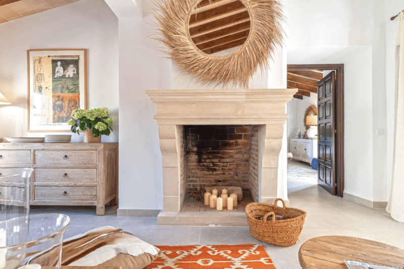 Rustic living room with a stone fireplace, wooden furniture, decorative mirror, and various decor elements such as a basket and potted plants.