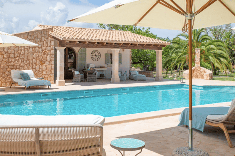 Luxury villa with a large swimming pool, covered patio area with outdoor furniture, and a stone exterior with a tiled roof.