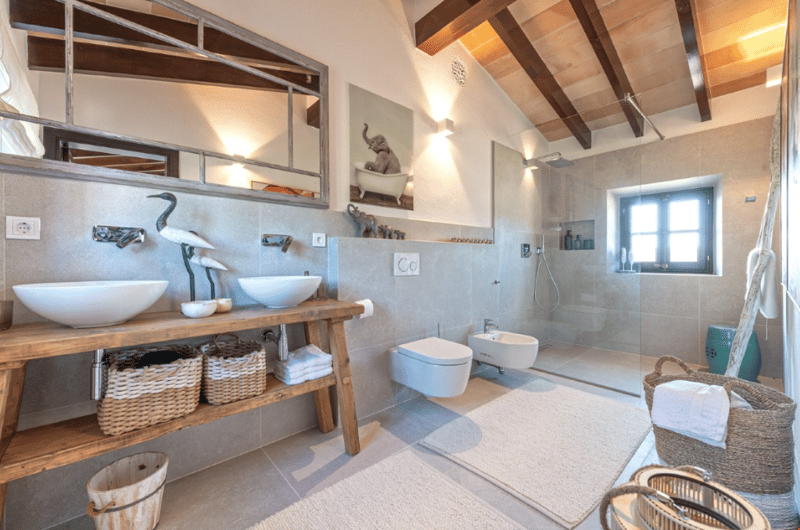 Spacious bathroom with wooden vanity, vessel sinks, tiled walls, and a walk-in shower. The room has exposed wooden beams on the ceiling and decorative elements like the elephant statue.