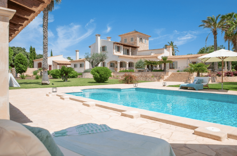 Large Mediterranean-style villa with a swimming pool, surrounded by lush greenery and palm trees. The villa has a terrace and balconies, and appears to be a luxurious and well-appointed property.
