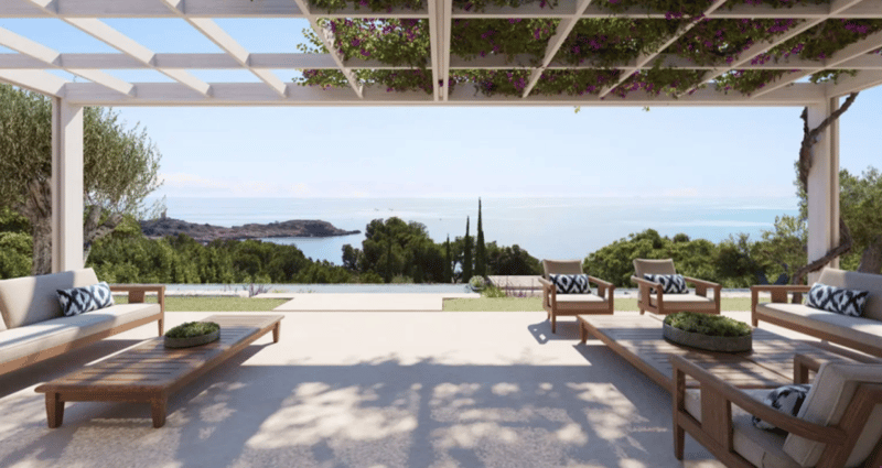 Covered outdoor patio with wooden furniture, overlooking a scenic coastal landscape with trees and water in the distance
