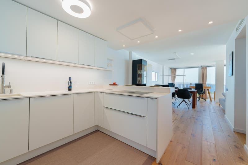 Modern, open-concept kitchen with white cabinets, quartz countertops, and hardwood floors. The kitchen is integrated with the living and dining areas, creating a spacious and bright living space. A dishwasher is visible on the kitchen counter.