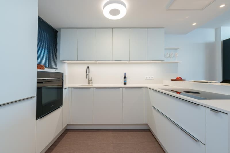 Modern kitchen with white cabinets, stainless steel appliances including a dishwasher, quartz countertops, and hardwood flooring