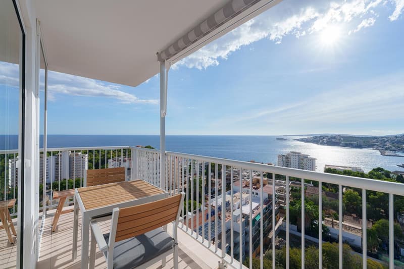 Spacious balcony with wooden furniture, overlooking a scenic coastal city and the ocean