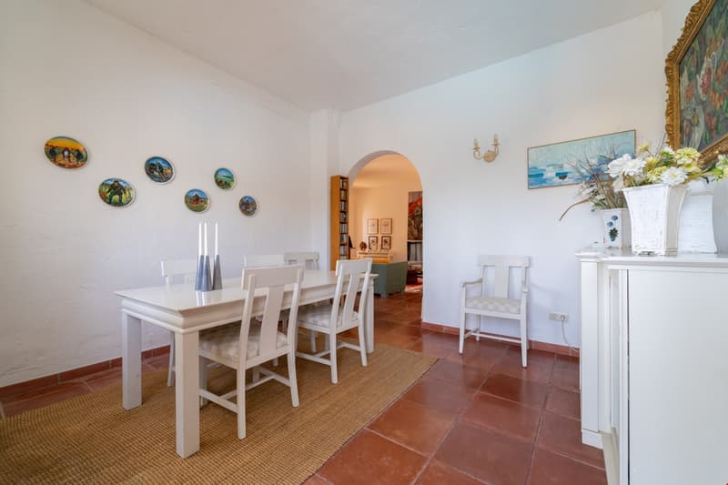 Spacious dining room with white table and chairs, decorative plates on the wall, fireplace, and a vase of flowers on a console table
