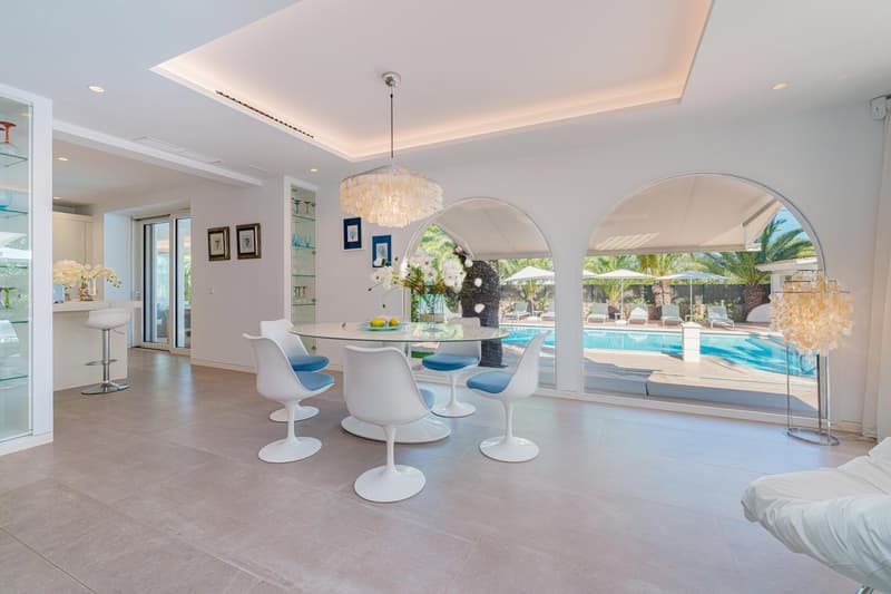Spacious open-plan living area with dining table and chairs, large windows overlooking a swimming pool, crystal chandelier, and modern decor