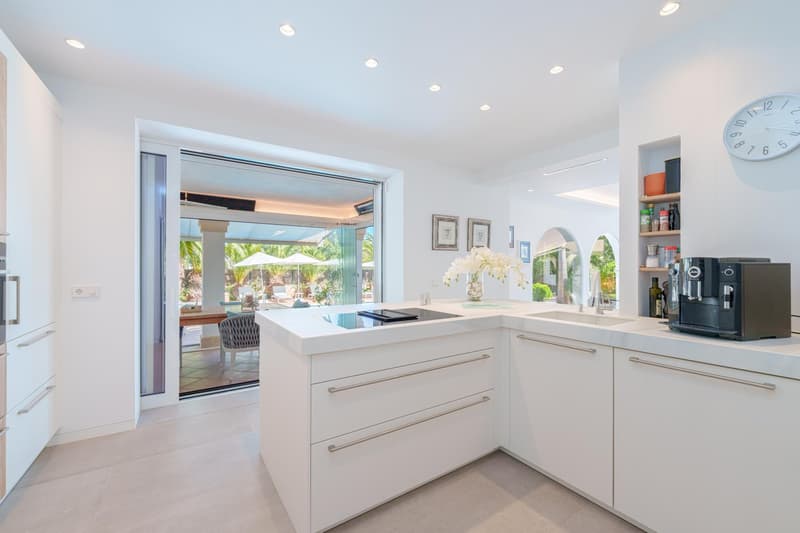 Spacious, modern kitchen with white cabinets, quartz countertops, and large sliding glass doors leading to a balcony or terrace. The kitchen also features a dishwasher and other high-end appliances.