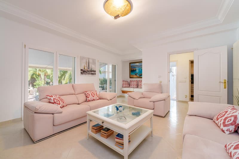 Spacious living room with large windows, pink sofas, glass coffee table, and decorative artwork on the walls