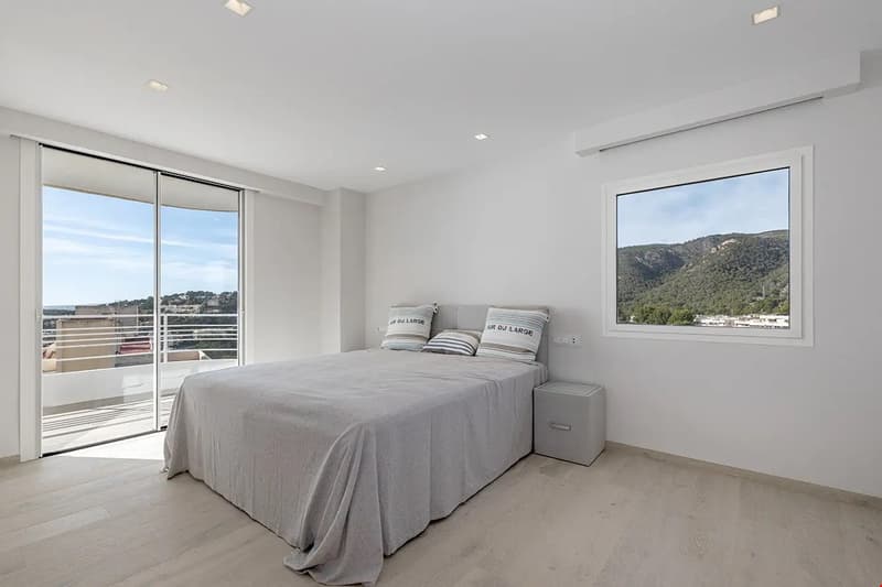 Spacious bedroom with large windows offering a scenic view, sliding glass doors leading to a balcony, grey bedding and decor, and a minimalist design