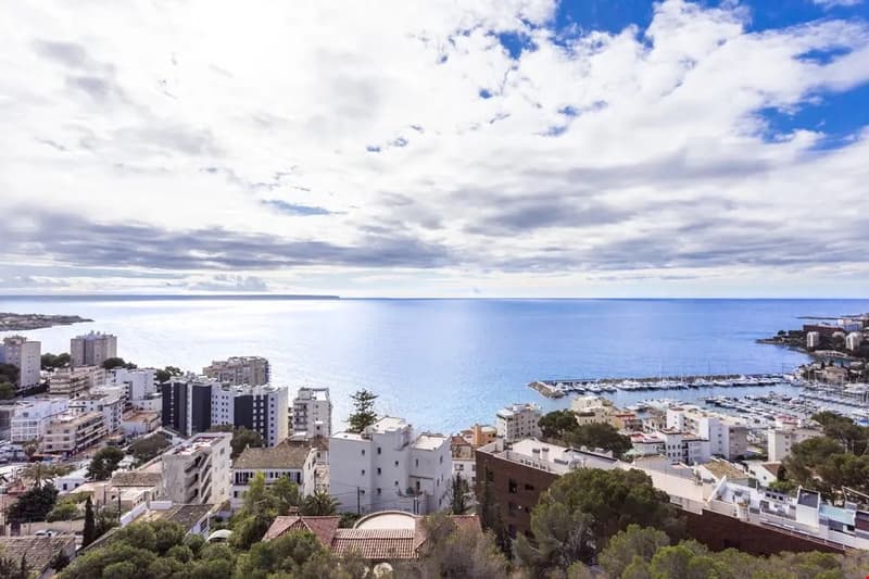 Aerial view of a coastal city with high-rise buildings, a harbor, and the blue ocean in the background. The sky is partly cloudy, creating a scenic landscape.
