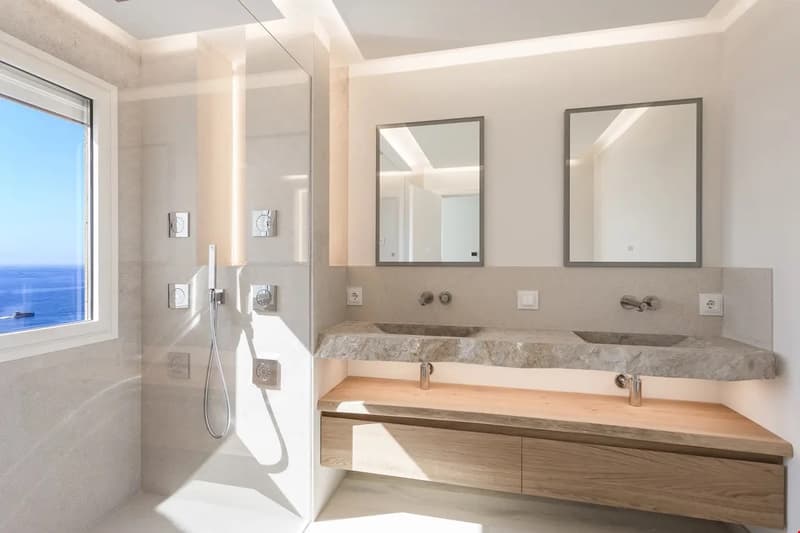Spacious bathroom with large windows offering a scenic view, double vanity with marble countertop, framed mirrors, and modern shower fixtures