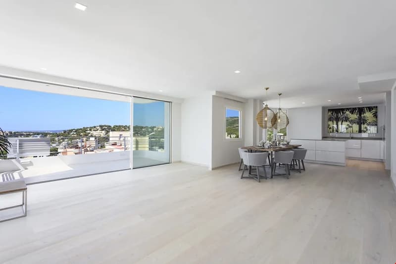 Spacious open-plan living area with large windows and sliding glass doors leading to a balcony with a scenic view, modern kitchen with white cabinets and island, dining area with a wooden table and chairs