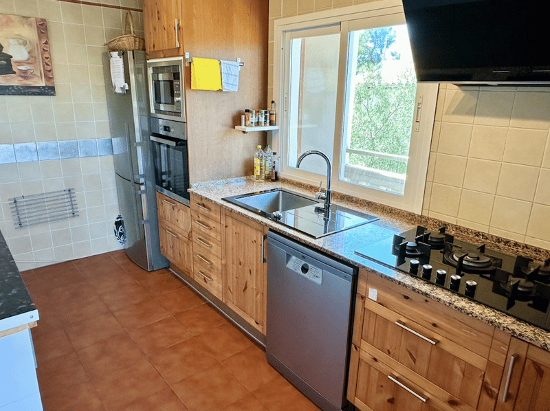 Spacious kitchen with wooden cabinets, granite countertops, stainless steel appliances including a dishwasher, and a large window overlooking the outdoors