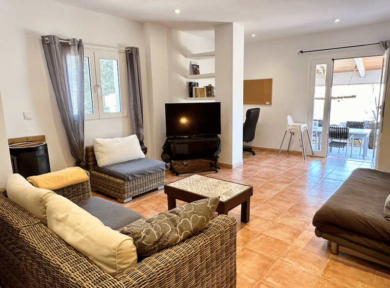 Spacious living room with tile flooring, wicker furniture, TV stand, and access to a balcony or terrace through large windows.