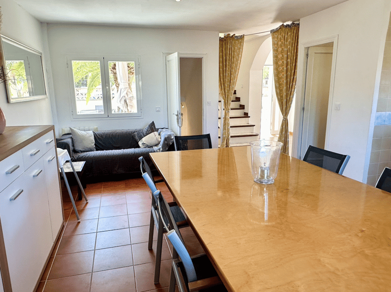 Open-plan living room with large windows, wooden dining table, black sofa, and yellow patterned curtains