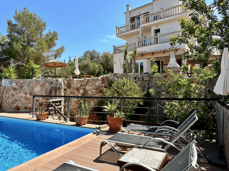 2-story Mediterranean-style villa with balconies, surrounded by lush greenery and a swimming pool in the foreground