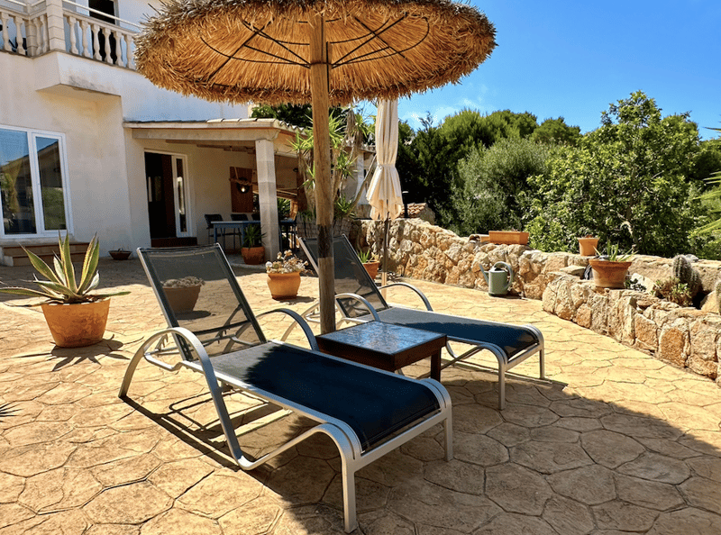 Outdoor patio with thatched umbrella, lounge chairs, potted plants, and stone paving
