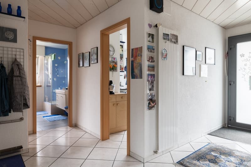 entryway with wooden entrance door, hallway with tiles, kitchen area visible, bathroom visible, open door to balcony, pictures on the wall
