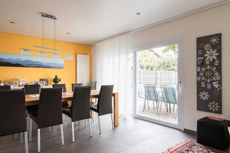 Dining room with dining table and chairs, yellow wall with artwork, sliding glass door to patio, rug on floor