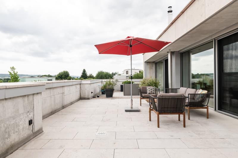 Outdoor terrace, wooden chairs, red umbrella, greenery, concrete walls, concrete floor, distant landscape