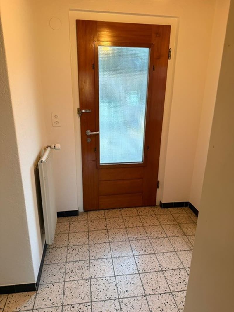 a room with a wooden door, tiled floor, and a white radiator