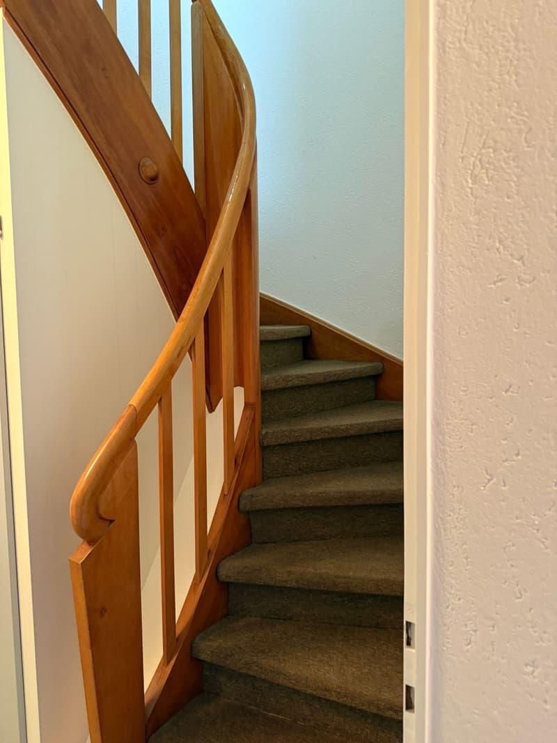 Wooden spiral staircase with beige carpeted steps and wooden railings.